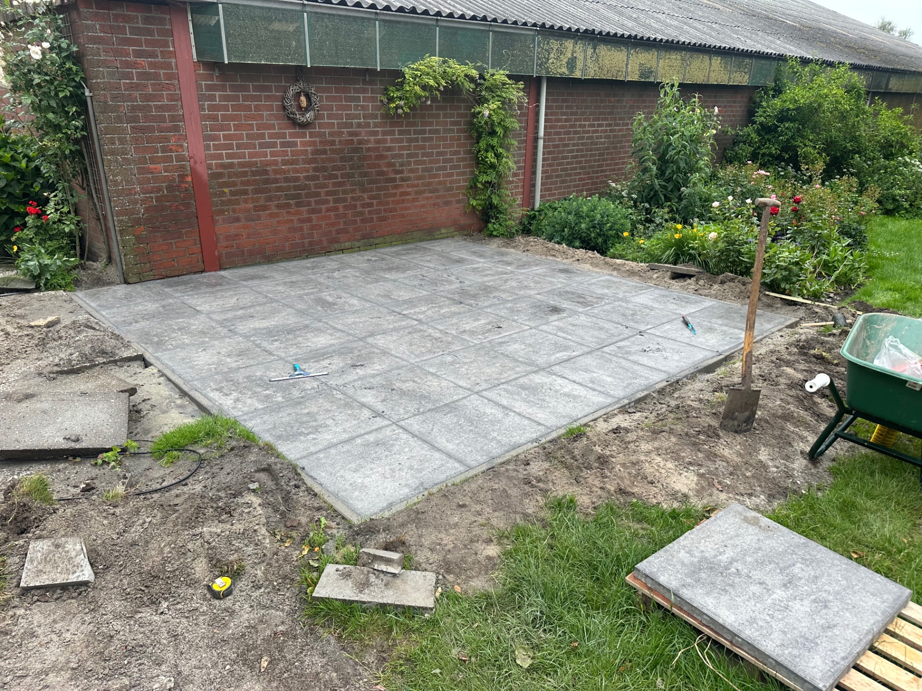 Nieuw gelegd terras van grote betontegels tegen een schuurmuur