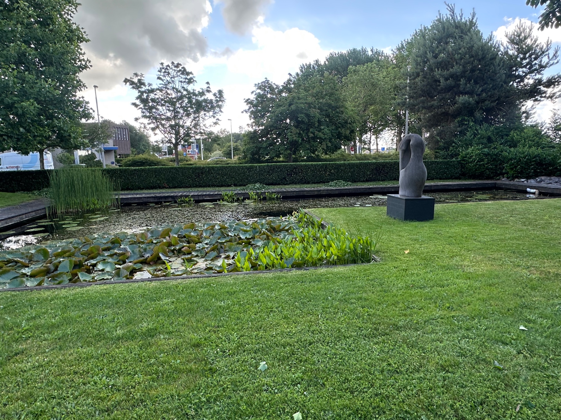 Vijver met waterplanten, strakke haag en egaal gazon bij een bedrijfstuin